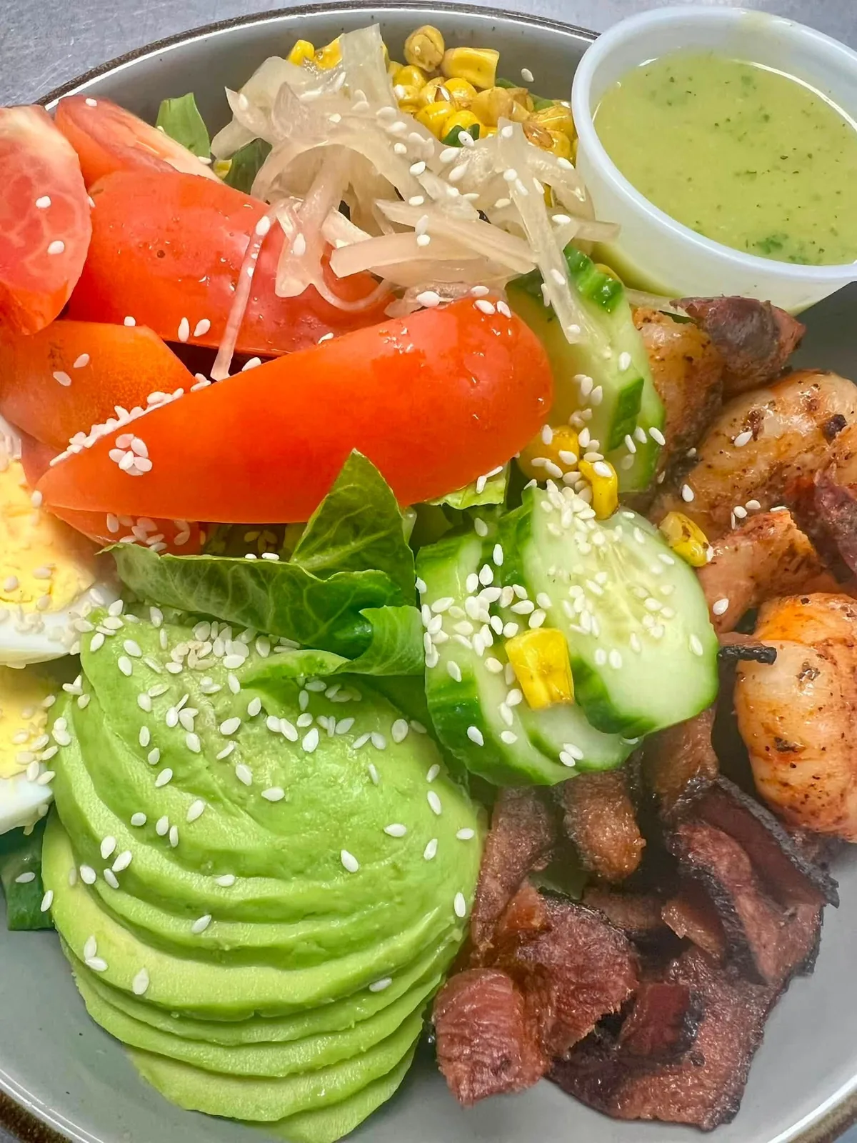 Grilled shrimp bowl with avocado, tomato, cucumber, corn, and greens