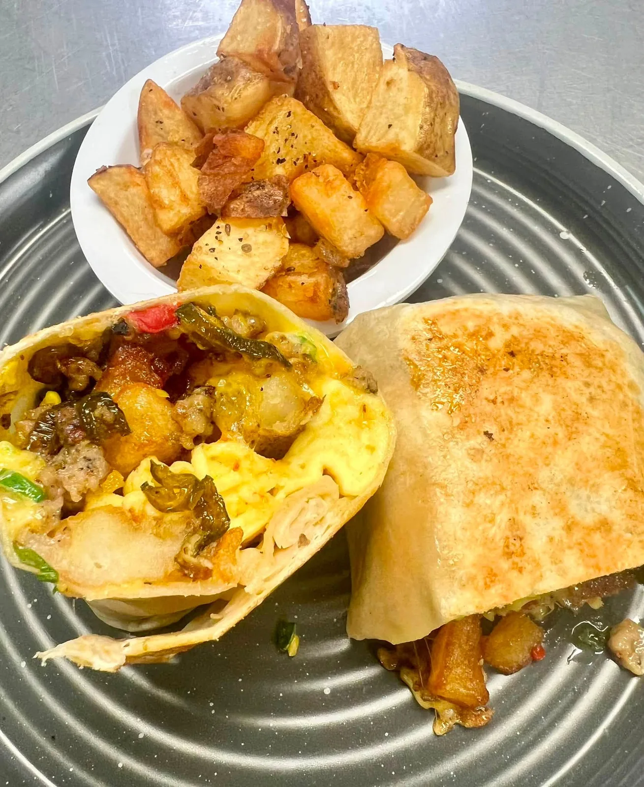 A loaded breakfast burrito with seasoned home fries on a diner platter